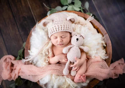 Ein niedliches Neugeborenes, das eine Teddybärenmütze trägt und einen kleinen Teddybären in der Hand hält.